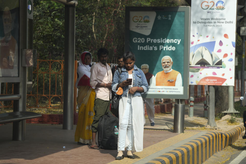 Commuters wait for local transportation in front of a G20 banners, in New Delhi, India, Wednesday, March 1, 2023. Fractured East-West relations over Russia's war in Ukraine and increasing concerns about China's global aspirations are set to dominate what is expected to be a highly contentious meeting of foreign ministers from the world's largest industrialized and developing nations this week in India. (AP Photo/Manish Swarup)