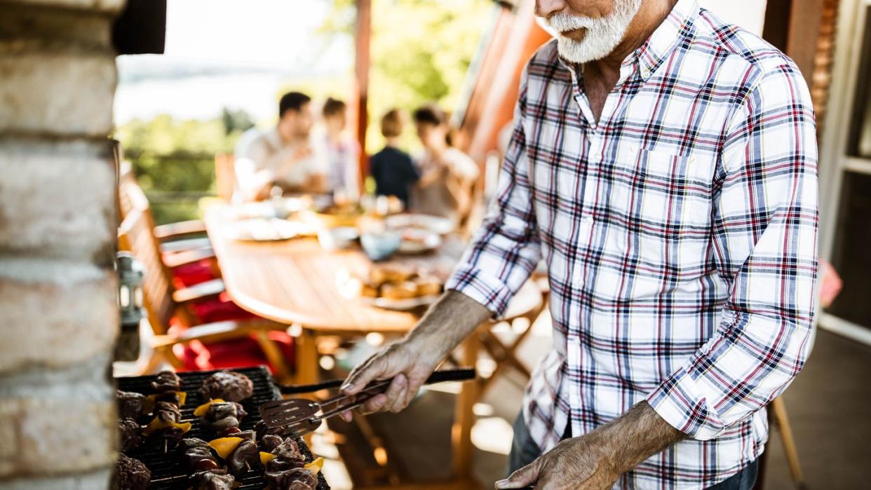 senior man making barbecue for his family's lunch on a terrace