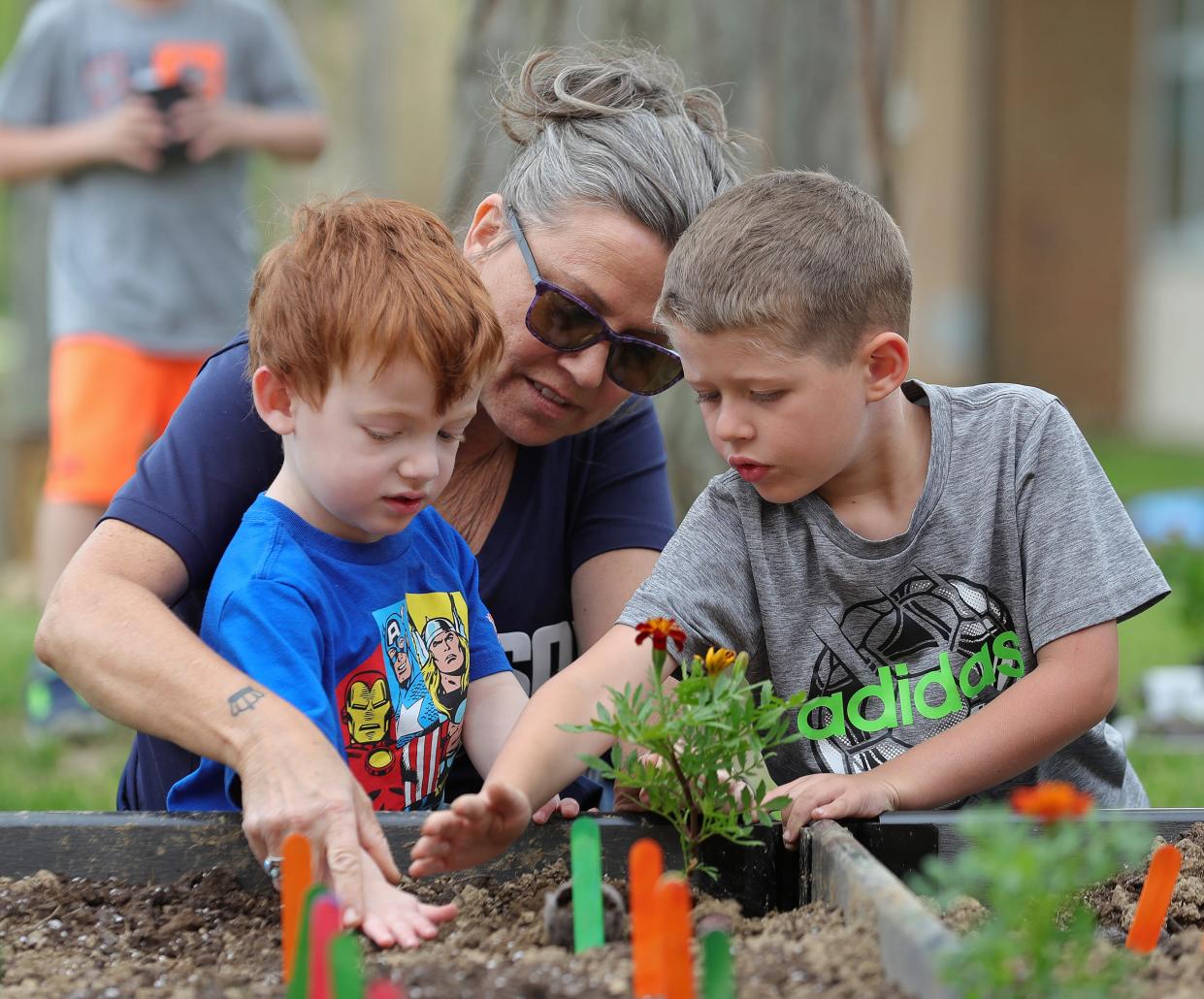 McDowell Early Learning School students Steven Weiss, left, and Connor Hartman, right, get help from aide Rena Tyrrell planting marigolds in the school’s sensory garden in Hudson.