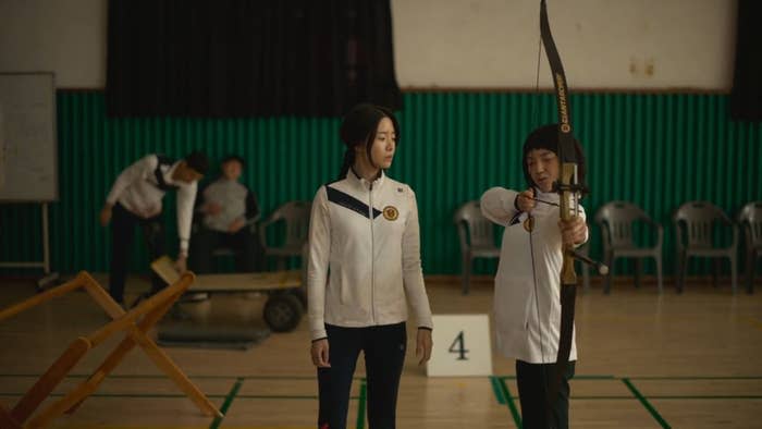 A girl practices archery while another girl standing next to her guides her