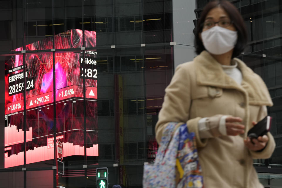 A woman walks across an intersection near monitors showing Japan's Nikkei 225 index at a securities firm in Tokyo, Thursday, Dec. 1, 2022. Shares have advanced in Asia after a rally on Wall Street spurred by the Federal Reserve chair's comments on easing the pace of interest rate hikes to tame inflation.((AP Photo/Hiro Komae)