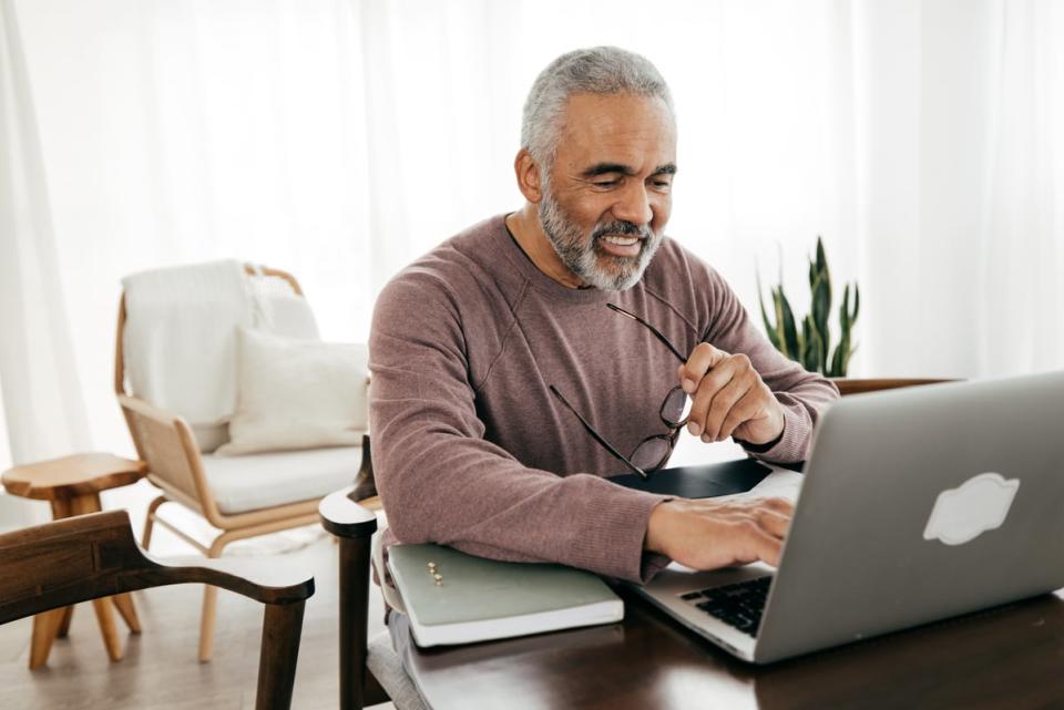 A person smiling while holding glasses and typing on a laptop computer. 