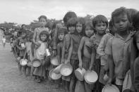 FILE - In this Jan. 9, 1975, file photo, bowls in hands, Cambodian refugee children wait their turn at a relief organization feeding station northwest of Phnom Penh, Cambodia. The youngsters and their families fled the Phnom Baseth area following Khmer Rouge insurgent raids nearby. The last surviving leaders of the communist Khmer Rouge regime that brutally ruled Cambodia in the 1970s were convicted of genocide, crimes against humanity and war crimes Friday, Nov. 16, 2018, by an international tribunal. (AP Photo/Tea Kim Heang aka Moonface, File)