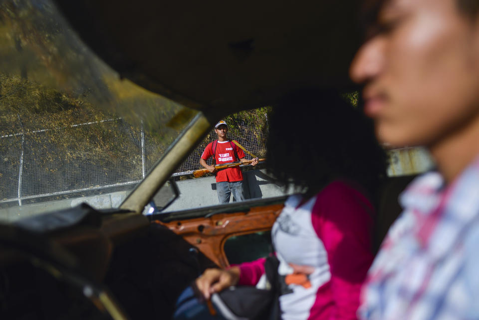 A couple drives past a member of the pro-government militias taking part in a foreign invasion drill in Caracas, Venezuela, Saturday, Feb. 15, 2020. Venezuela's President Nicolas Maduro ordered two days of nationwide military exercises, including the participation of civilian militias. (AP Photo/Matias Delacroix)