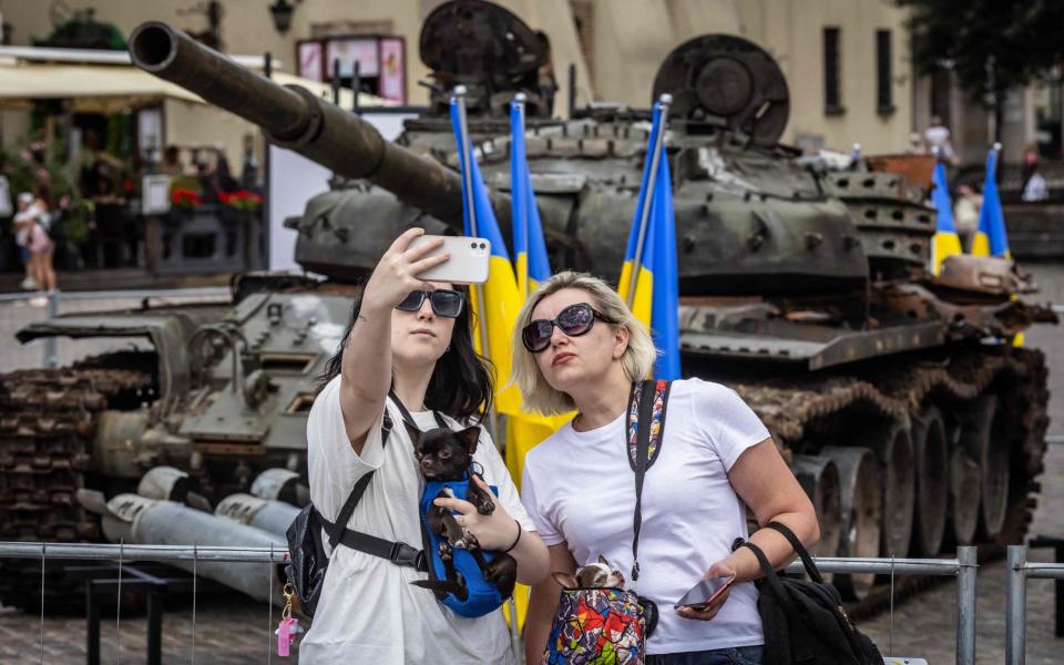 Two women pose for a selfie in front of a destroyed Russian T-72 tank - WOJTEK RADWANSKI/AFP via Getty Images