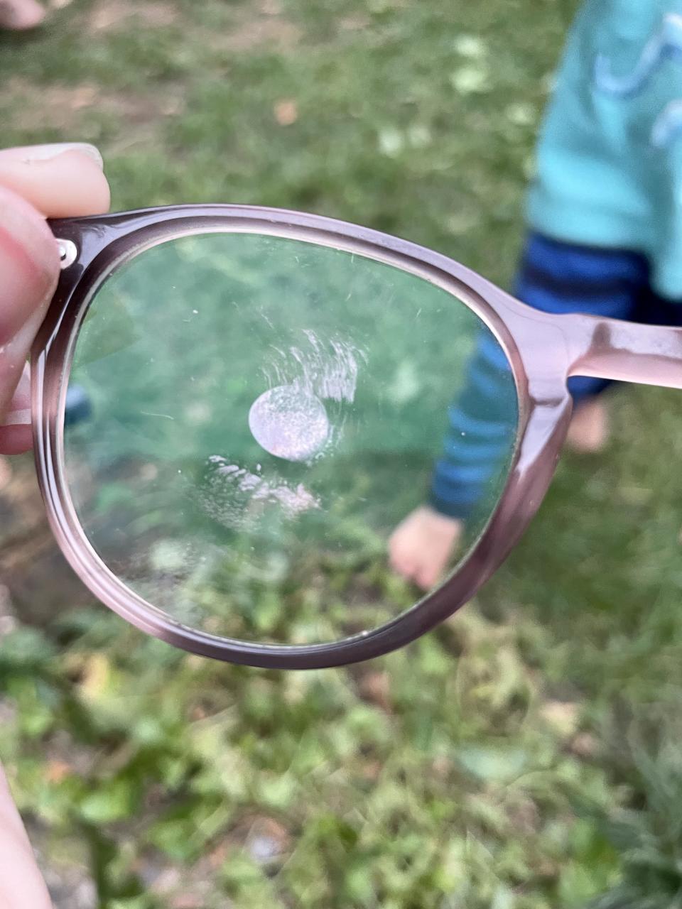 Smudged eyeglasses lens held near a child playing outside on grass