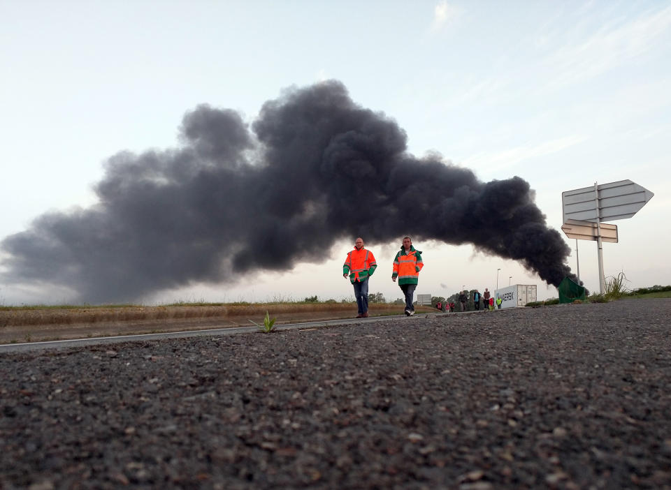 <p>Two union activists in fluorescent vests walk toward the Normandie Bridge outside of Le Havre, western France, during a blockade action, May 26, 2016. The cloud of black smoke is from burning tires. French Prime Minister Manuel Valls says he is open to "improvements and modifications" in a labor bill that has sparked intensifying strikes and protests, but will not abandon it. (Raphael Satter/AP) </p>