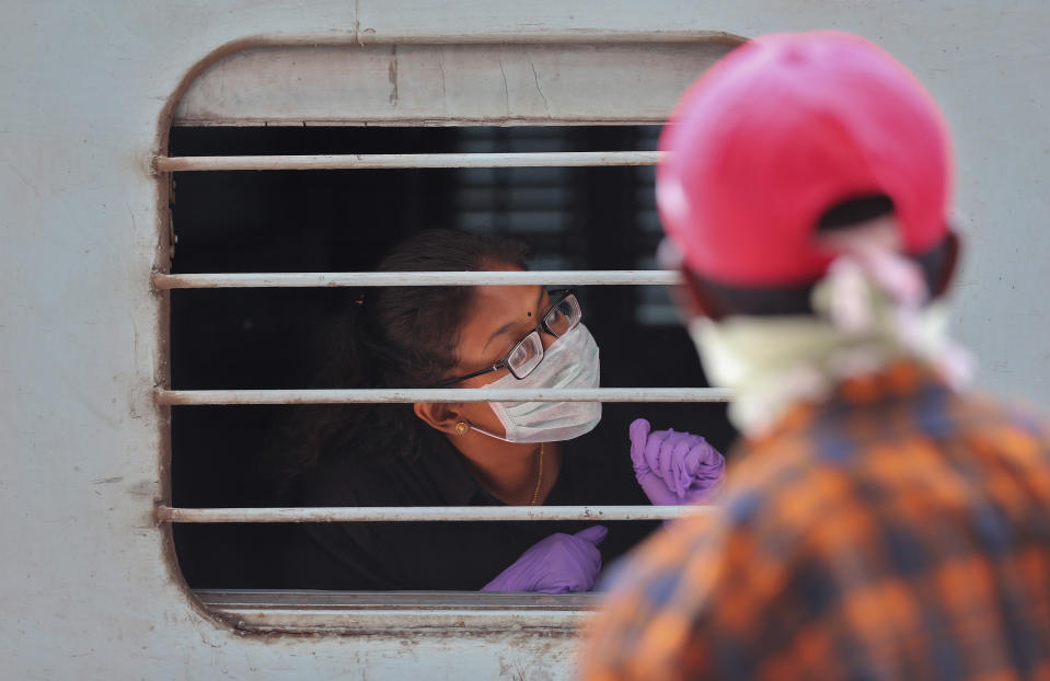 An Indian passenger wearing face mask and gloves as a precaution against COVID-19 peeps out of a train window at Secunderabad Railway Station in Hyderabad, India, Saturday, March 21, 2020. For most people, the new coronavirus causes only mild or moderate symptoms. For some it can cause more severe illness. (AP Photo/Mahesh Kumar A.)