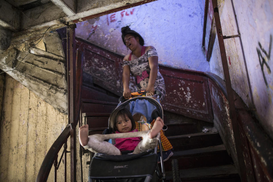 In this March 18, 2020 photo, Nilu Asca, a 24-year-old single mother, struggles to pull a stroller holding her 2-year-old daughter Darleth up a flight of stairs, inside a building nicknamed “Luriganchito” after the country’s most populous prison, in Lima, Peru. Darleth has been diagnosed with hip dysplasia and must wear a spica cast. She and her mother are one of 44 families who reside in one of the small rooms of the deteriorating building, just a few blocks from the presidential palace. (AP Photo/Rodrigo Abd)