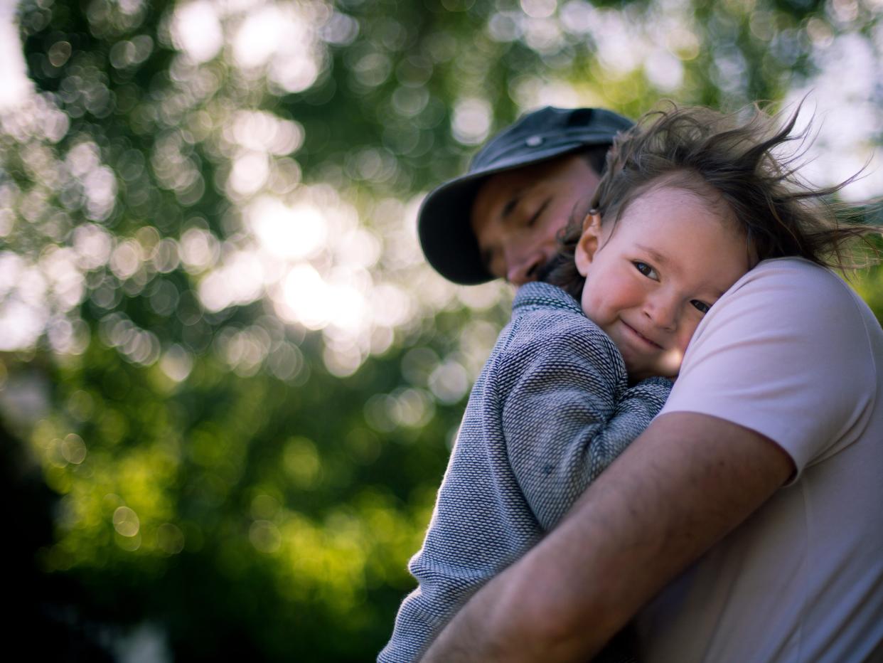 2 year old is being held by dad while the wind messes with his hair