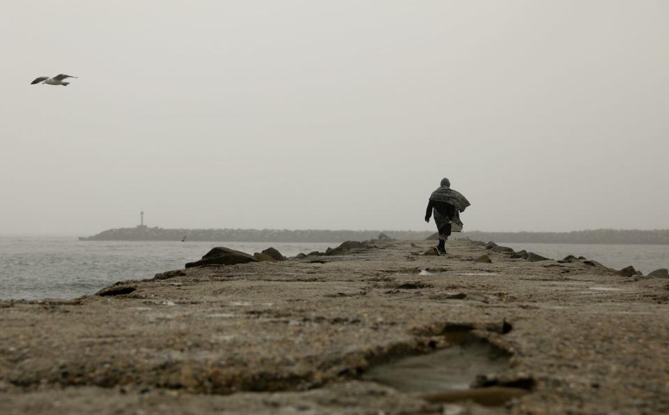 A lone figure walks on a jetty in low clouds.