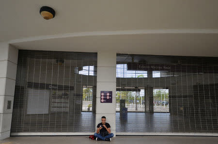 A man looks on his mobile phone outside at a closed metro station after Puerto Rico Electric Power Authority (PREPA), the island's power company, said Wednesday that a major power line failure in southern Puerto Rico cut electricity to almost all customers, in San Juan, Puerto Rico April 18, 2018. REUTERS/Willin Rodriguez