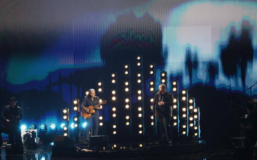 Tracy Chapman plays guitar and sings with Luke Combs in front of light bulbs on the Grammy Awards stage