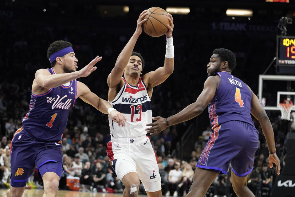 Washington Wizards' Jordan Poole (13) maneuvers between Phoenix Suns' Devin Booker (1) and Chimezie Metu (4) during the first half of an NBA basketball game in Phoenix, Sunday, Dec. 17, 2023. (AP Photo/Darryl Webb)