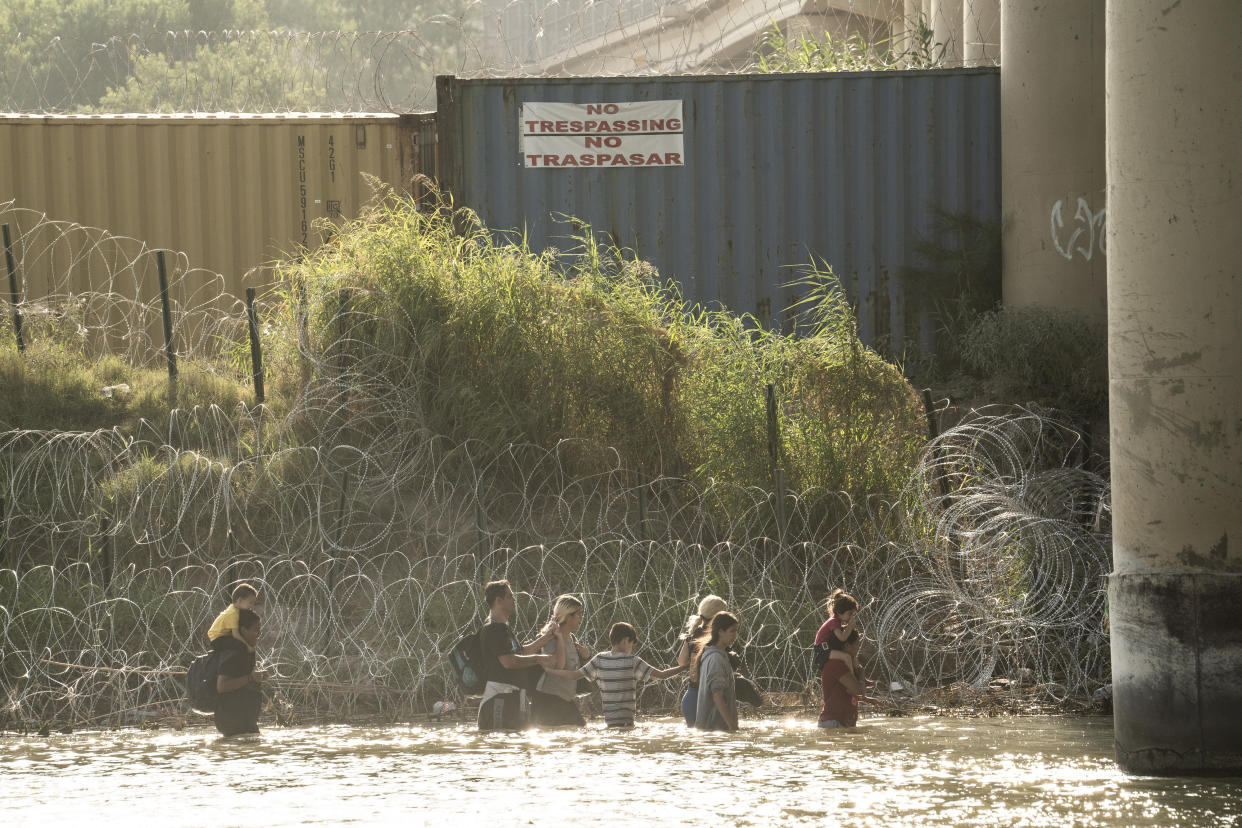 Algunos migrantes, vistos desde Piedras Negras, México, caminan a lo largo del río Bravo en busca de una abertura en la concertina en Eagle Pass, Texas, el 19 de julio de 2023. (Go Nakamura/The New York Times)
