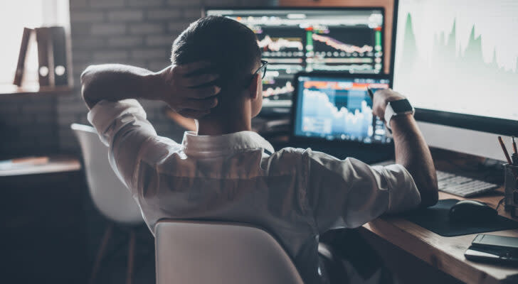 Businessman looking at stock charts on computer screen with one hand on the back of his head and the other hand holding a pen