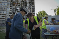 Local residents get free meals from volunteers against the background of their apartment house, damaged in the Russian rocket attack, in Kharkiv, Ukraine, Friday, June 2, 2023. (AP Photo/Andrii Marienko)