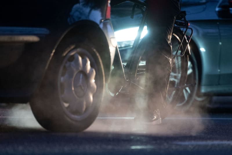 A cyclist stands next to a diesel-powered Mercedes car whose exhaust fumes are visible in the cold morning air. A ruling is expected on 28 March in a class action suit against German carmaker Mercedes-Benz in relation to the long-running scandal over emissions of nitrogen oxides. The Stuttgart Higher Regional Court has scheduled a hearing in the matter for 9 am. Marijan Murat//dpa