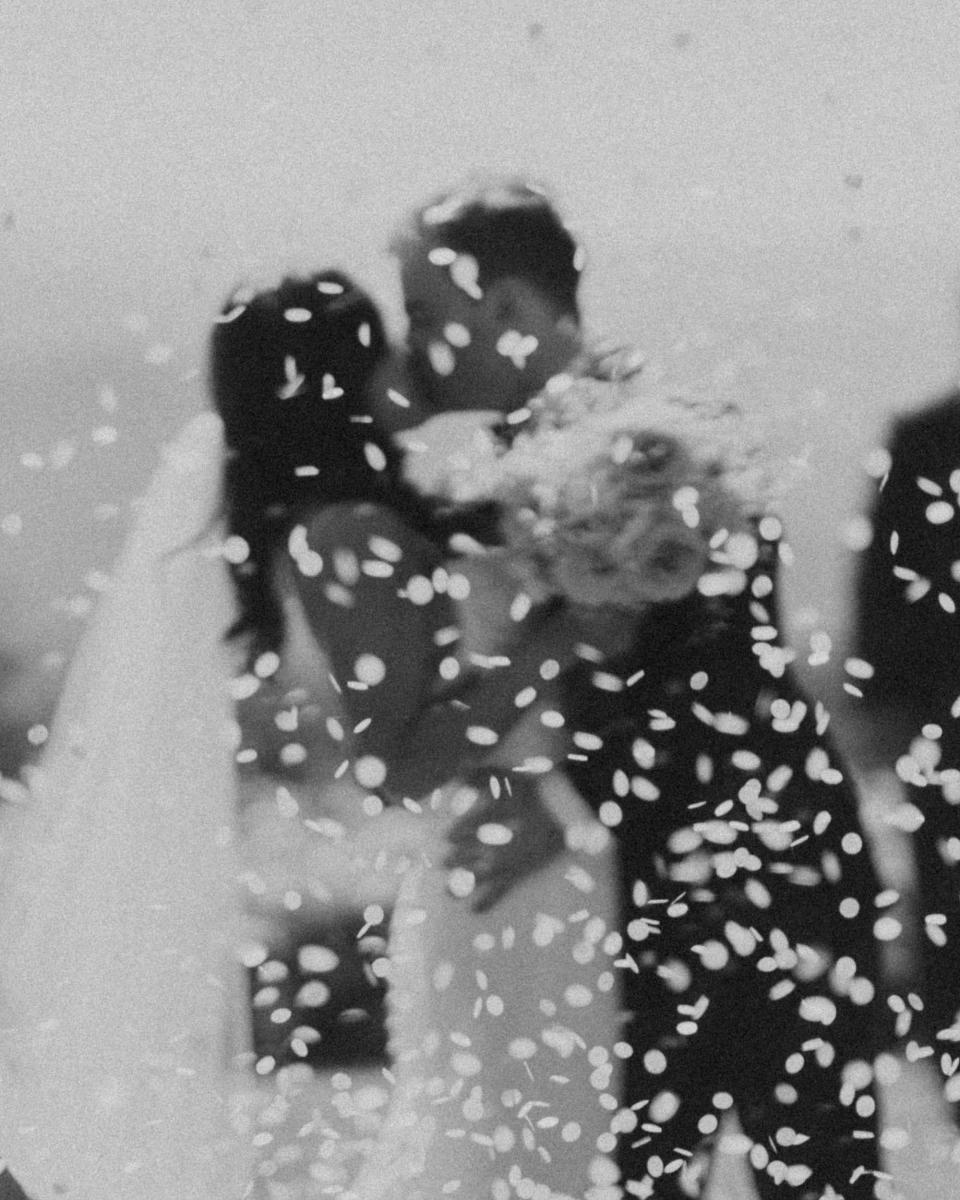 A blurry shot of a groom dipping and kissing a bride as flower petals explode around them.