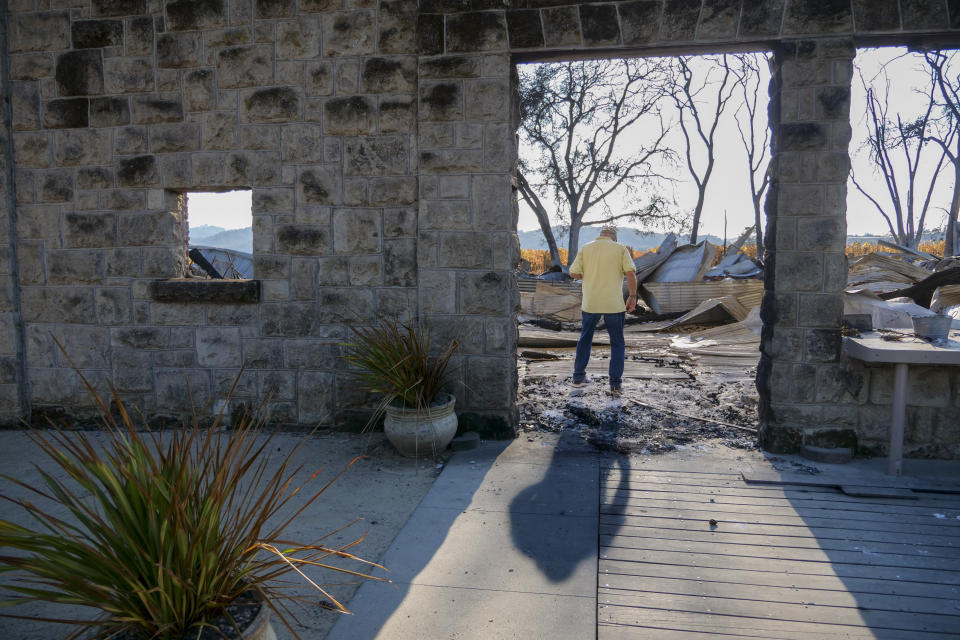 In this Tuesday, Nov. 5, 2019, photo, Ken Wilson, owner of the Soda Rock Winery, surveys debris from the winery's main building in Healdsburg, Calif. The 1869 building, destroyed by the Kincade wildfire, was originally a general store and post office. After the fire,Wilson and his staff immediately reopened with free wine tastings to begin their recovery. Signs on the nearby roadside announced wine tastings: "RECOVERY BEGINS!" Many have stopped in. "This is what I call resiliency!" one customer said as he arrived. Wilson, a Canadian who moved to Sonoma County in 1979, explained that this was how he started tastings with his first winery in 1998, "a plank and two barrels and we were in business. (AP Photo/Lacy Atkins)