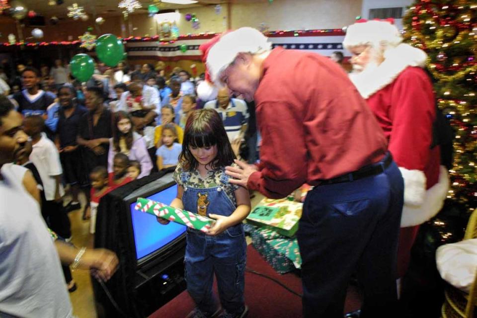 To Broward, 12/14/03. Photo by Candace West/Herald Staff. Robert L. Agee VFW Post 1966, 350 SW 25th Street, Ft. Lauderdale. U.S. Sen. Bob Graham, D-Fla., holds his 395th work day, giving away toys to children of service people who are now stationed in Iraq. Graham will be serving as Santa’s helper. Here Rebecca Sanchez, age 5 of Hallandale leaves happy with a gift from Graham and Santa. The kids in the background are waiting in line for their turn with santa. Candace West/Herald Staff