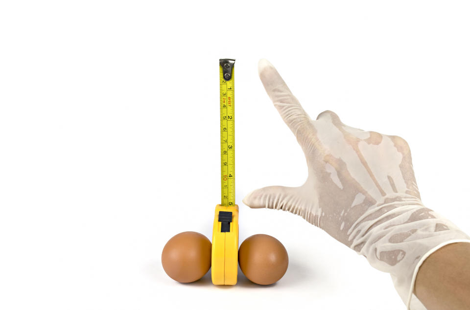 A hand wearing a surgical glove measures 5 inches on an extended tape measure resting between two eggs.