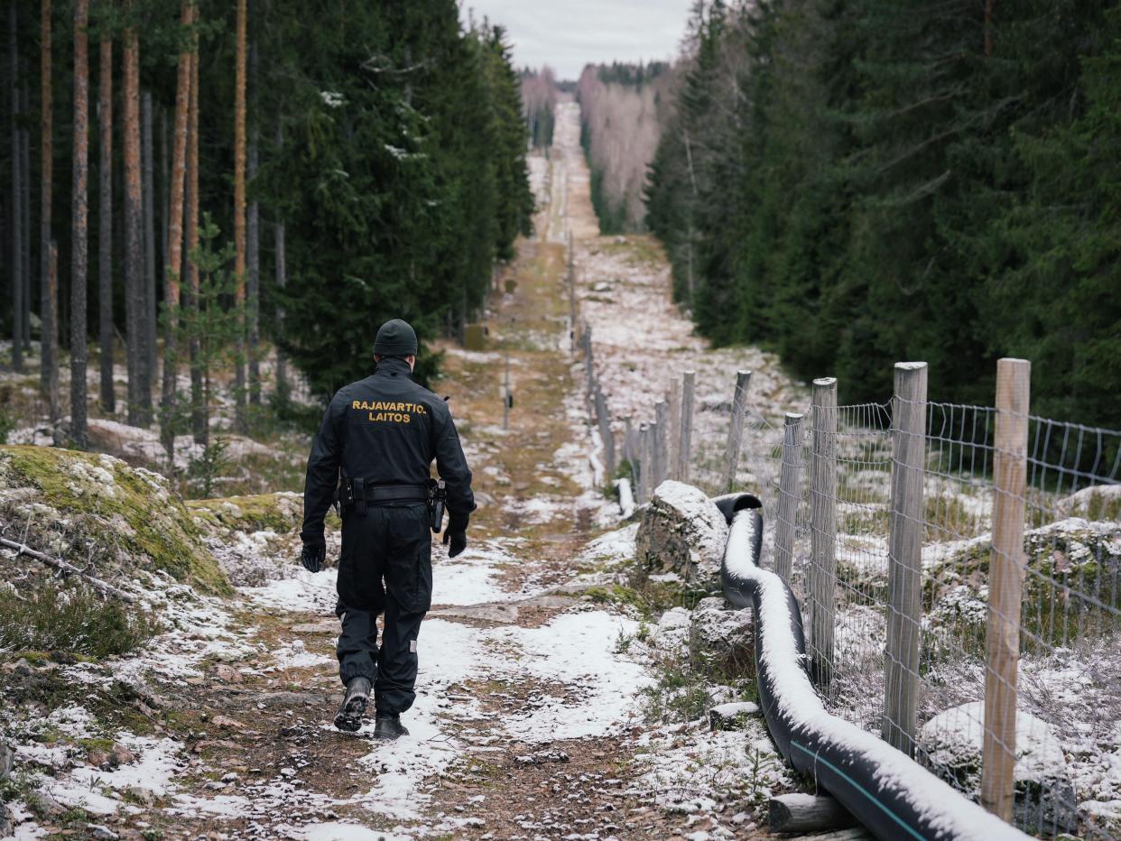 A border guard officer walks along a fence marking the boundary area between Finland and Russia.