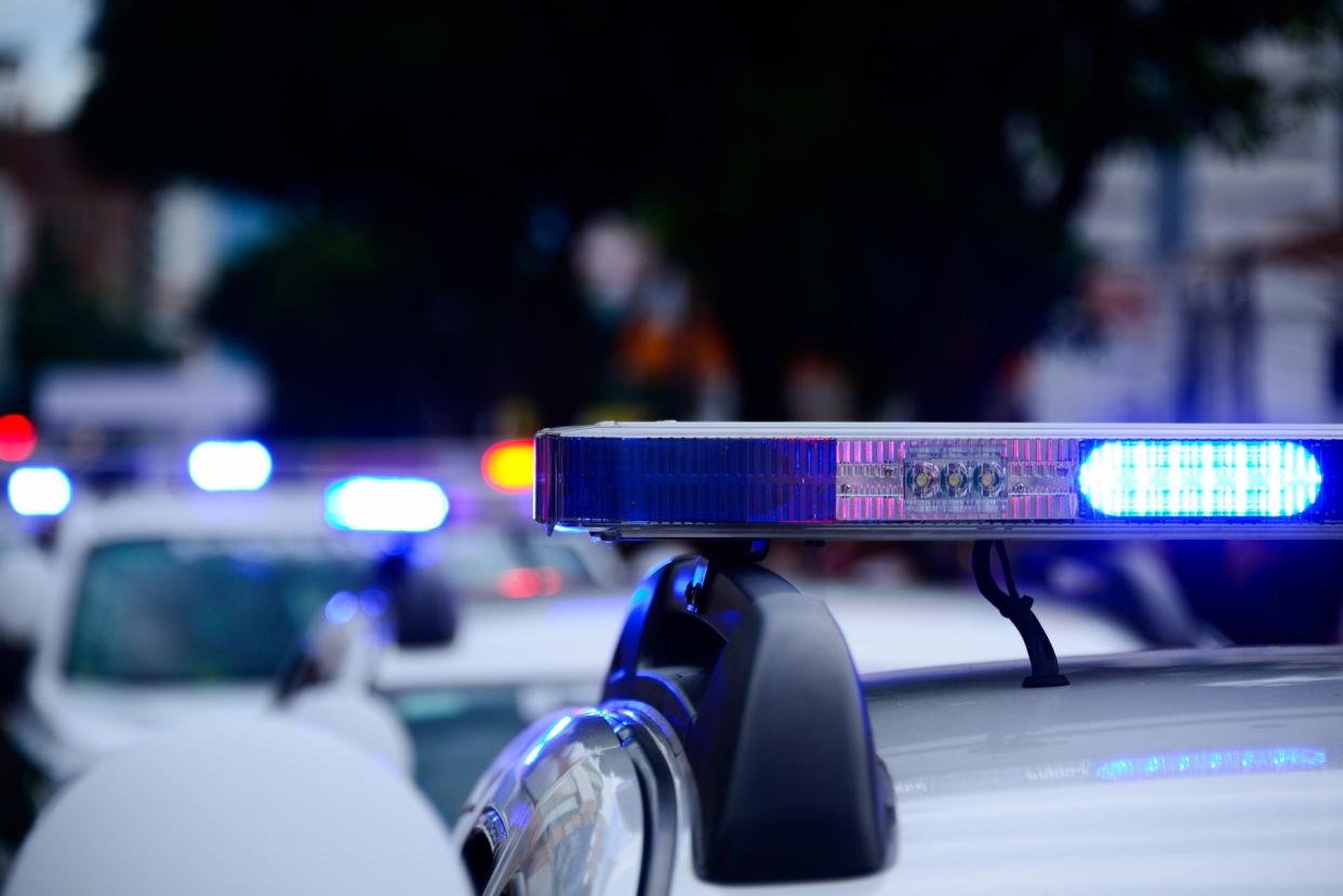 Blue lights flash atop a police car, with several other vehicles also flashing in the background.