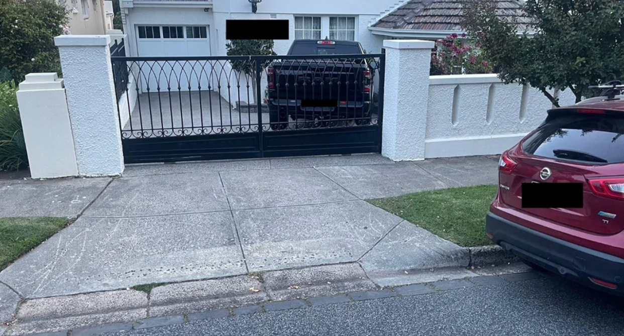 The red Nissan is parked close to the edge of the driveway with a black RAM car parked behind a gate in the driveway. 