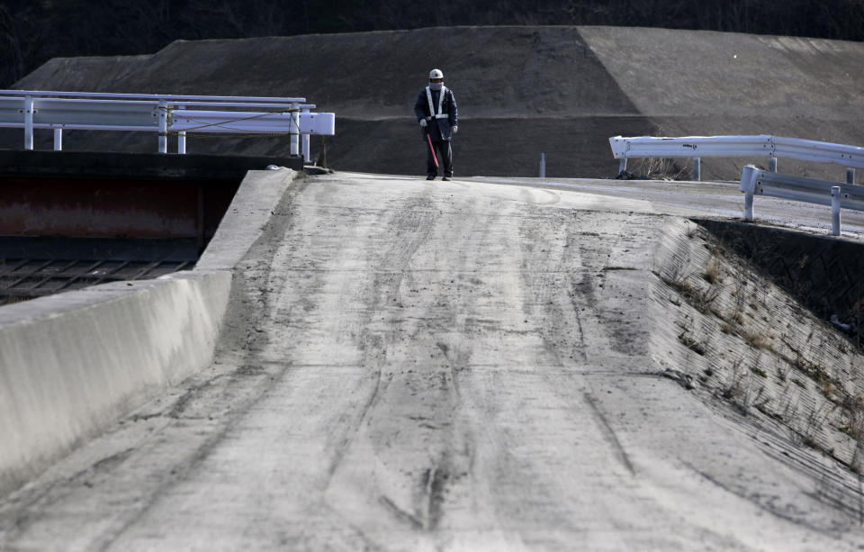 In this Tuesday, March 4, 2014 photo, a worker stands on an intersection of a make-shift access road leading to construction sites in Otsuchi, Japan. Construction has only begun at two of 10 planned sites in Otsuchi and further down the coast. (AP Photo/Junji Kurokawa)