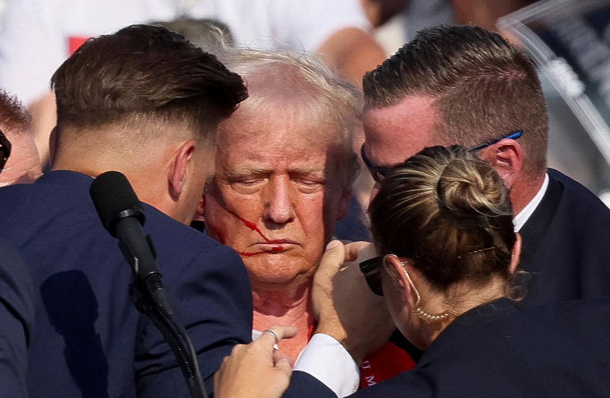 Trump, with apparent blood on the right side of his face, is assisted by the Secret Service after gunfire.