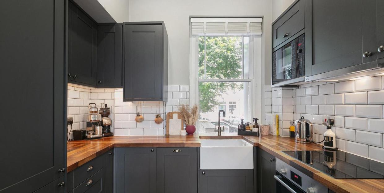 a modern city kitchen with grey cabinets and wooden worktops and a window beyond