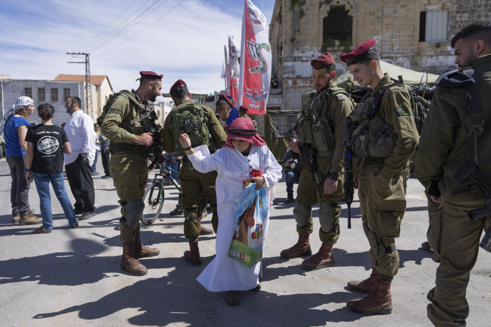 Jewish settlers dressed in costumes celebrate the Jewish holiday of Purim as soldiers secure the march in the West Bank city of Hebron, Tuesday, March 7, 2023. Hebron is a flashpoint city where several hundred hard-line Israeli settlers live in heavily guarded enclaves amid some 200,000 Palestinians. The settlers each year hold a parade on Purim – a Jewish holiday marked by costumes and revelry that commemorates the Jews' salvation from genocide in ancient Persia, as recounted in the biblical Book of Esther. (AP Photo/Ohad Zwigenberg)