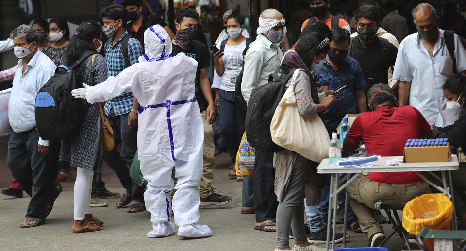 A health worker in protective suit directs arriving passengers towards the COVID-19 testing counter outside a train station in Bengaluru, India.