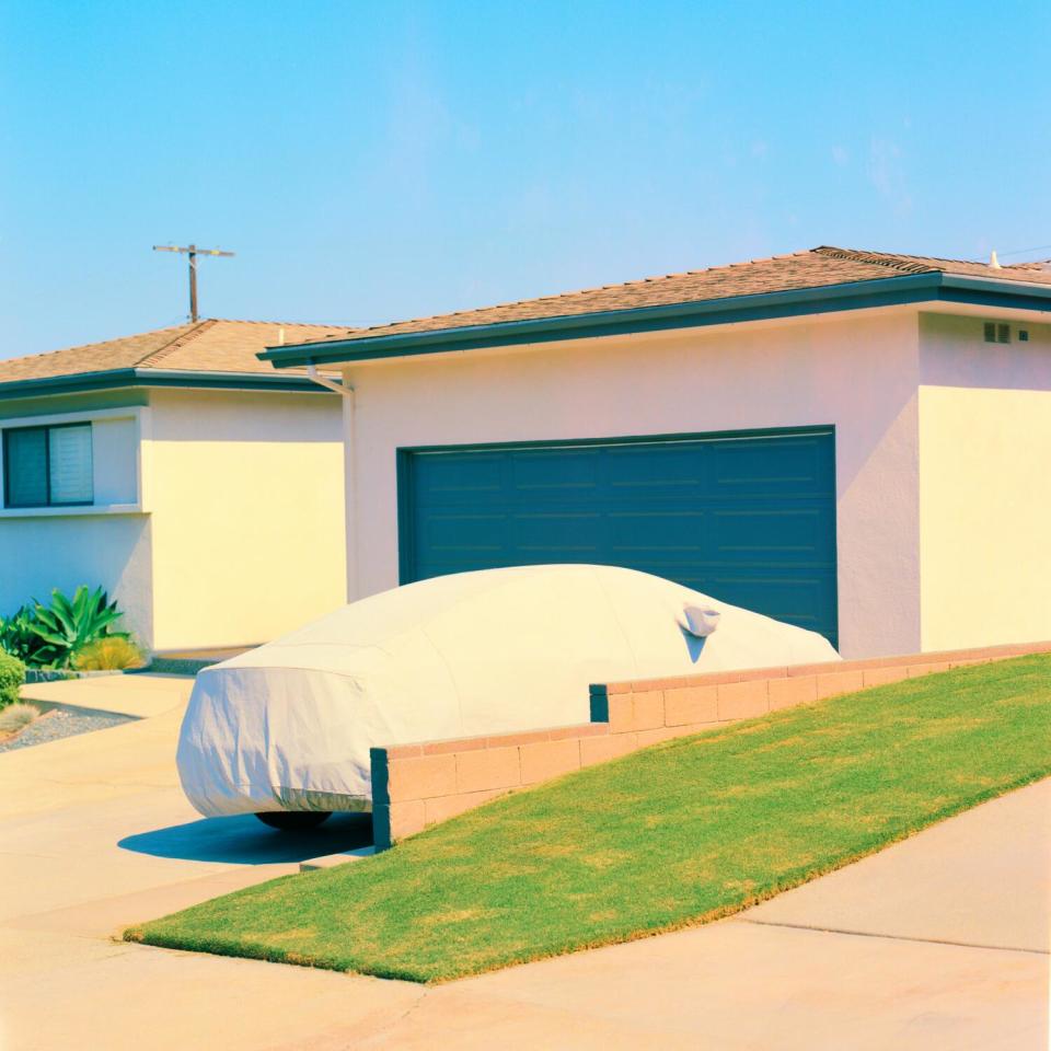 A photo of a covered car parked outside a house garage.