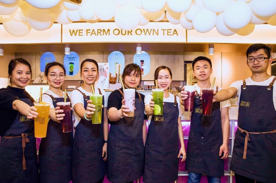 Seven staff members at the Gotcha Fresh Tea restaurant in Melbourne are standing in a line holding different kinds of fresh tea.