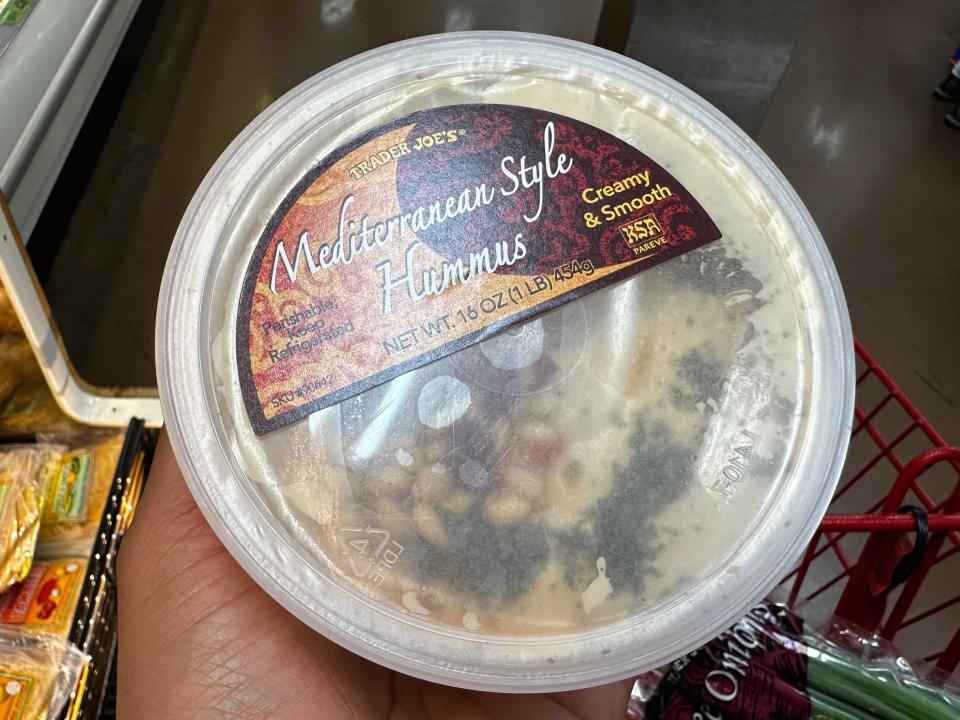 hand holding a container of mediterranian-style hummus from trader joe's