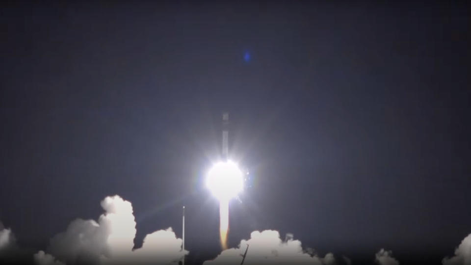 a bright white plume of fire lifts off at night above a cloud of smoke. a white rocket is just barely visible above the flames