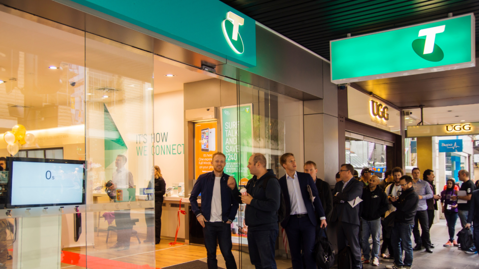 A line of people wait outside a Telstra store.