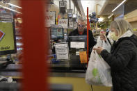 Cashier George Wallace, of Quincy, Mass., center, works behind a plastic shield as a shopper, right, places groceries in a cart, Thursday, March 26, 2020, at a grocery store, in Quincy. Grocery stores across the U.S. are installing protective plastic shields at checkouts to help keep cashiers and shoppers from infecting each other with the coronavirus. (AP Photo/Steven Senne)