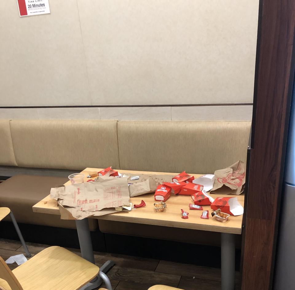 An untidy fast-food booth with scattered wrappers, containers, and cups on the table and seating area