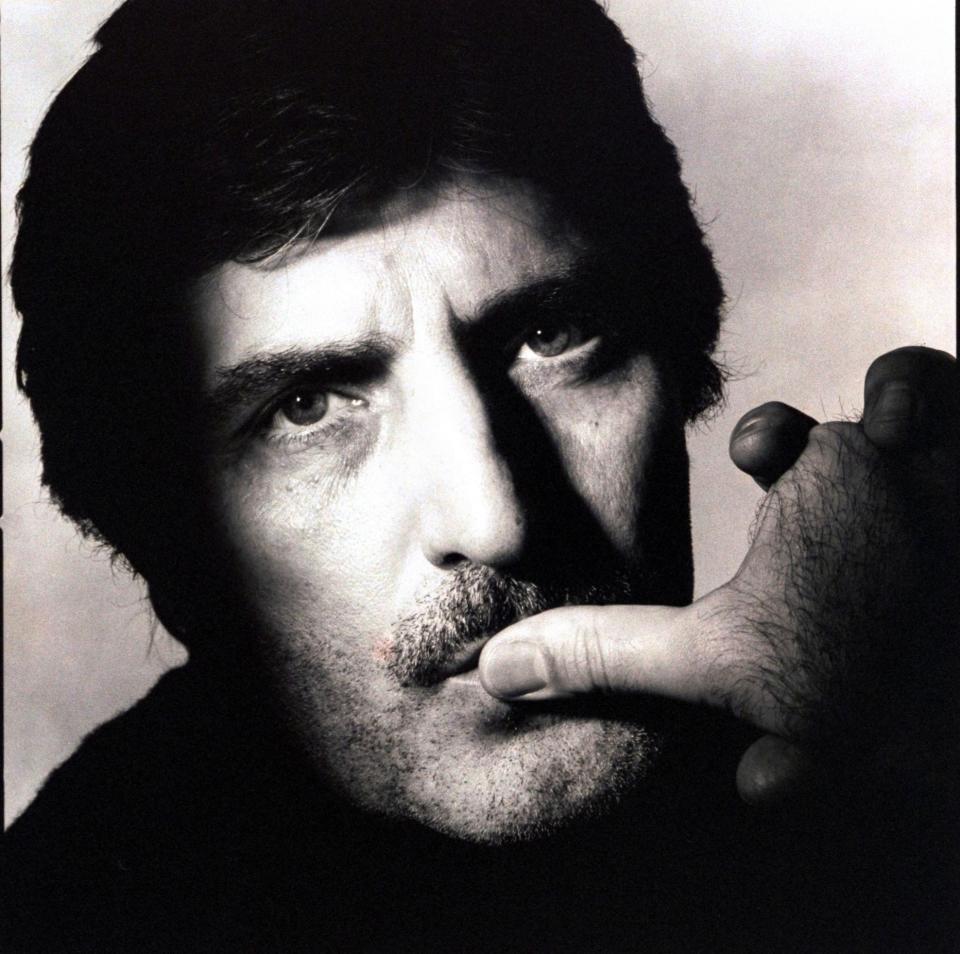 Headshot of fashion designer, Emanuel Ungaro, with moustache and a three-day beard, with his thumb on his lips, with a serious look