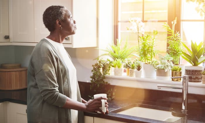 Person standing in a kitchen looking out a window.