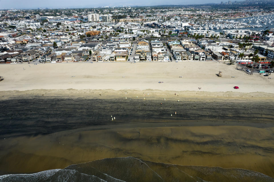 In this aerial image taken with a drone, workers in protective suits clean the contaminated beach after an oil spill in Newport Beach, Calif., on Wednesday, Oct. 6, 2021. Some of the crude oil that spilled from a pipeline into the waters off Southern California has been breaking up naturally in ocean currents, a Coast Guard official said Wednesday as authorities sought to determine the scope of the damage. (AP Photo/Ringo H.W. Chiu)
