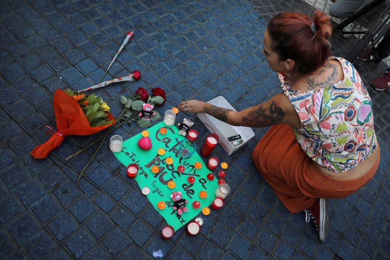 A woman places a candle on a placard, reading in Spanish and Catalan