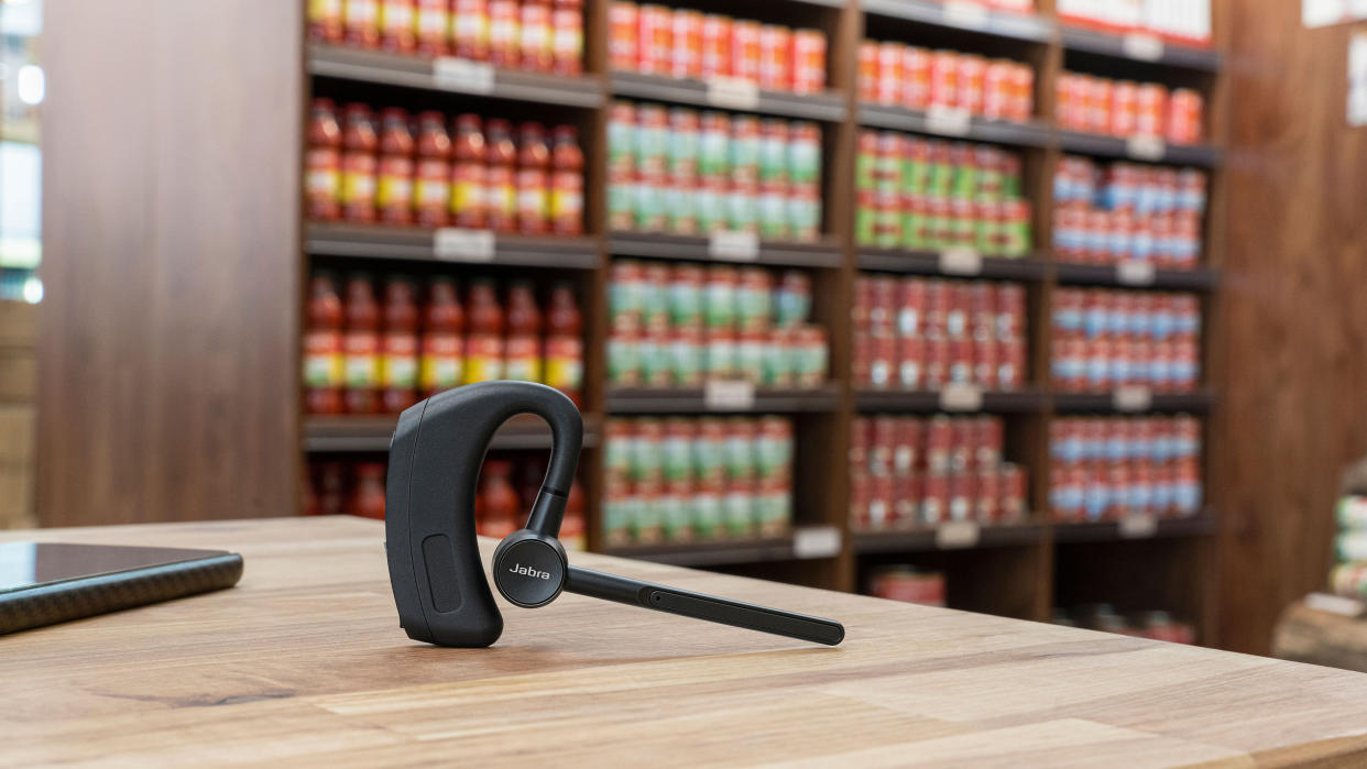  The new Jabra Perform 45 headset in black sitting on a wood table in front of stocked shelves. 