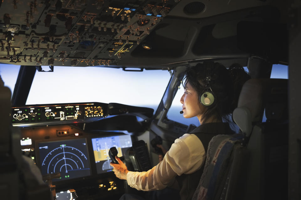 A female pilot is navigating an airplane cockpit, focused on the controls and instruments, symbolizing professional aviation work