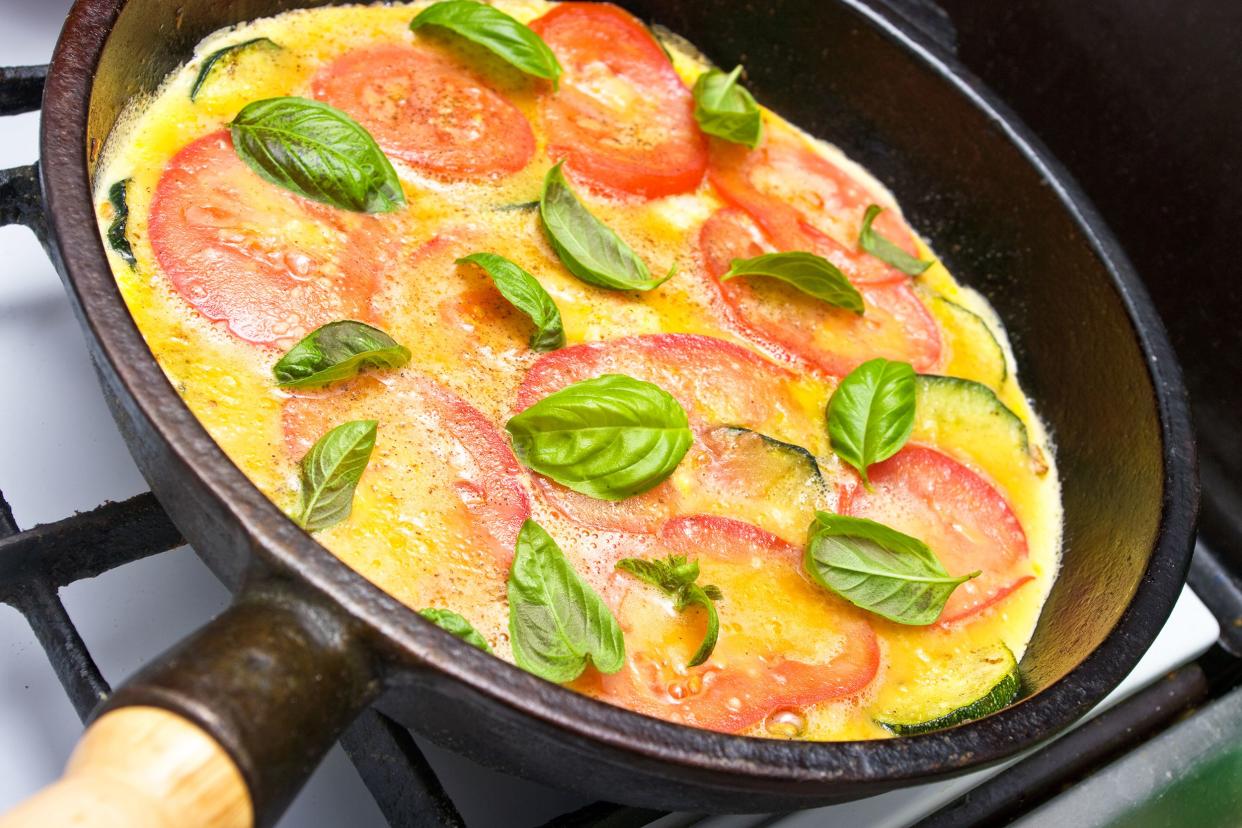 Focus on tomato and herb omelet in a cast iron skillet on a black burner of a stove with a blurred background