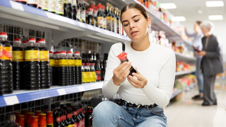 Young woman choosing soy sauce at supermarket