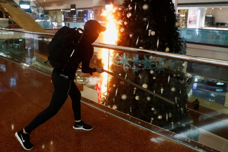 A protester is seen next to a burning Christmas tree at Festival Walk mall in Kowloon Tong, Hong Kong